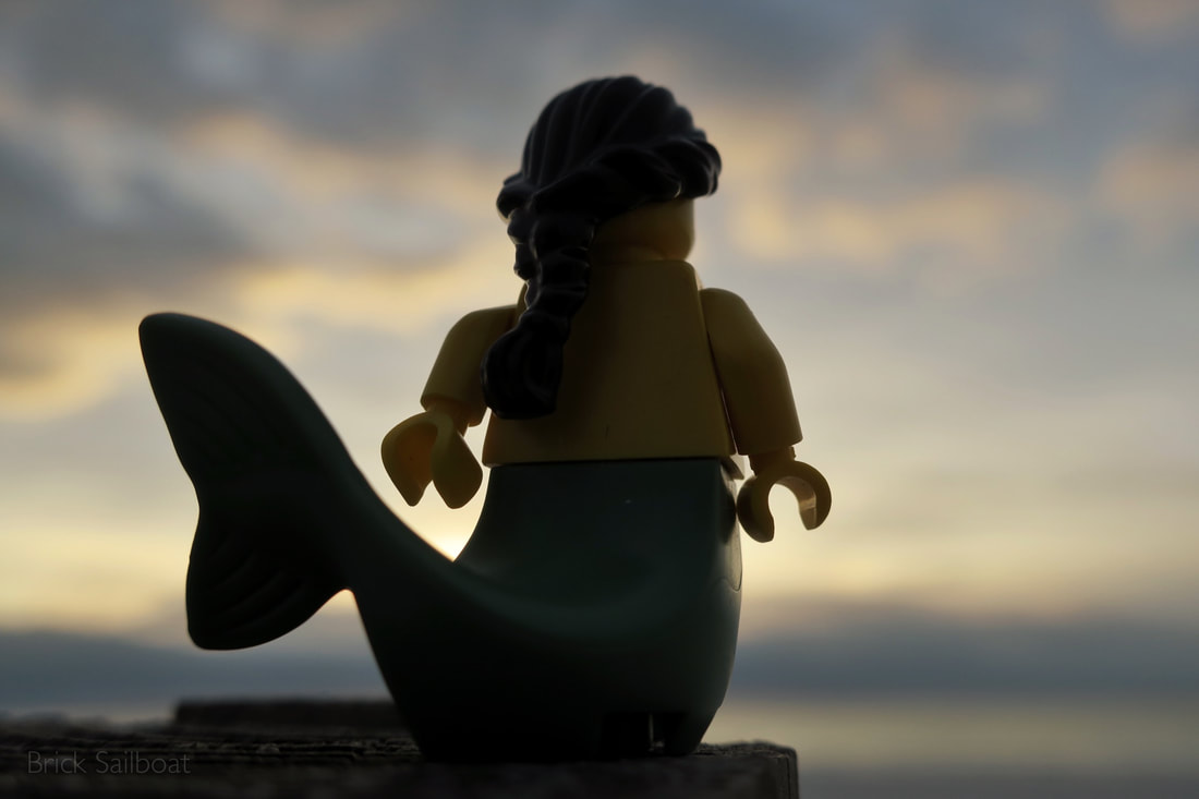 A LEGO mermaid looking out to sea at sunset