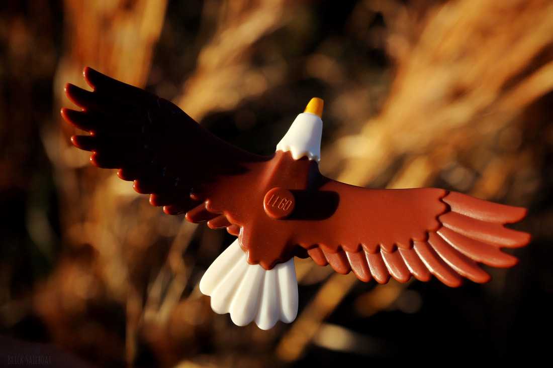 A LEGO bald eagle flies over a field.